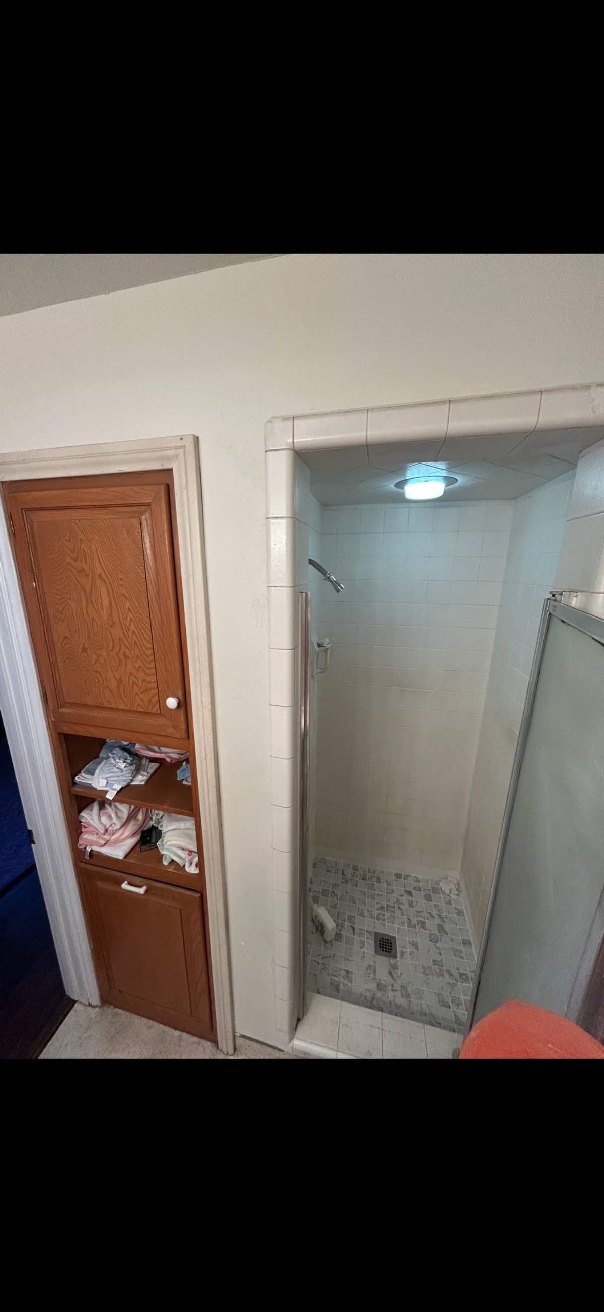 Bathroom interior with walk-in shower stall, glass door, wooden linen cabinet, and white tiled walls