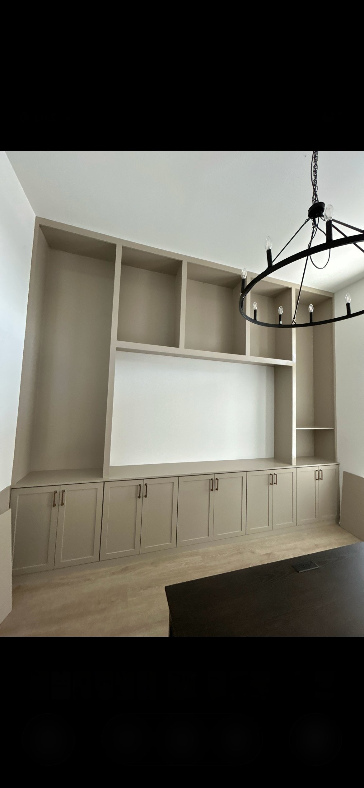 Modern living room with floor-to-ceiling built-in shelving unit in light beige, lower cabinetry, central display area, and a black wrought iron chandelier