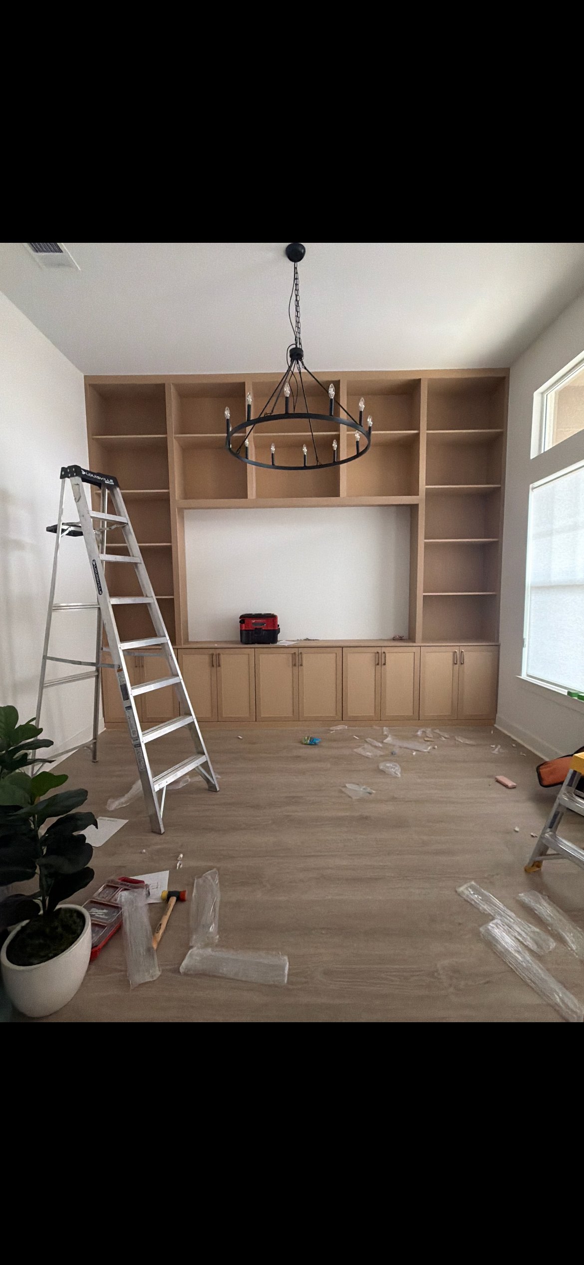 Interior room under renovation with wooden built-in shelving, pendant chandelier, stepladder, and plastic drop cloths on the floor