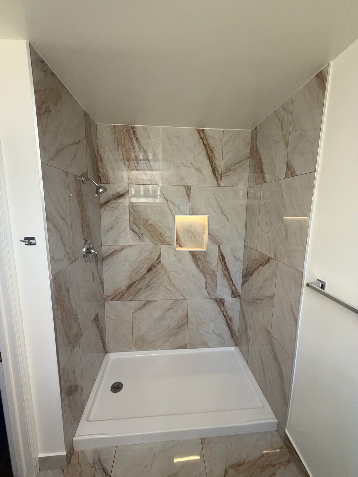 Modern bathroom shower enclosure with marble-effect tile walls, white base pan, chrome fixtures, and built-in niche